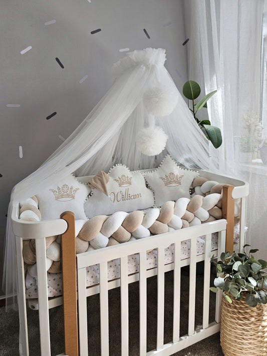 Baby crib with white bedding, decorative pillows, and a canopy in a nursery setting.